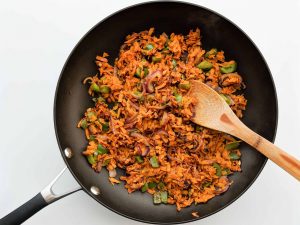 shredded sweet potatoes in pan with peppers and onions